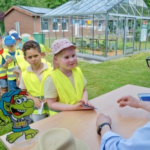 Bürgermeister Dr. Tobias Lehberg drückt, assistiert vom Energietroll Energix, im Energiewelten-Garten im Bioenergiepark den letzten Stempel in die Laufkarten der Kita-Vorschulkinder, die dann ihren "Forscherpass für Klimaschützer" nach vier Lern- und Erlebnismodulen komplett haben.