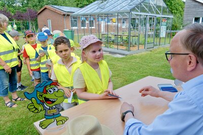 Bürgermeister Dr. Tobias Lehberg drückt, assistiert vom Energietroll Energix, im Energiewelten-Garten im Bioenergiepark den letzten Stempel in die Laufkarten der Kita-Vorschulkinder, die dann ihren "Forscherpass für Klimaschützer" nach vier Lern- und Erlebnismodulen komplett haben.