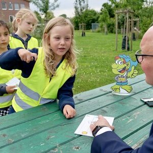Bürgermeister Dr. Tobias Lehberg drückt, assistiert vom Energietroll Energix, im Energiewelten-Garten im Bioenergiepark den letzten Stempel in die Laufkarten der Kita-Vorschulkinder, die dann ihren "Forscherpass für Klimaschützer" nach vier Lern- und Erlebnismodulen komplett haben.