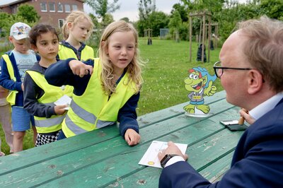 Bürgermeister Dr. Tobias Lehberg drückt, assistiert vom Energietroll Energix, im Energiewelten-Garten im Bioenergiepark den letzten Stempel in die Laufkarten der Kita-Vorschulkinder, die dann ihren "Forscherpass für Klimaschützer" nach vier Lern- und Erlebnismodulen komplett haben.
